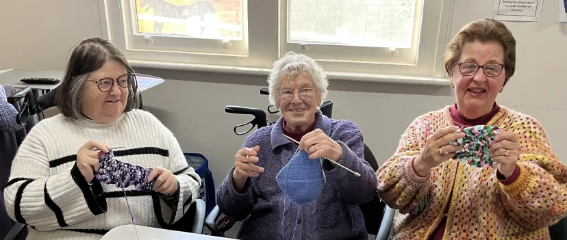 Three members holding up their knitting and crochet at a Neighbourhood Centre group